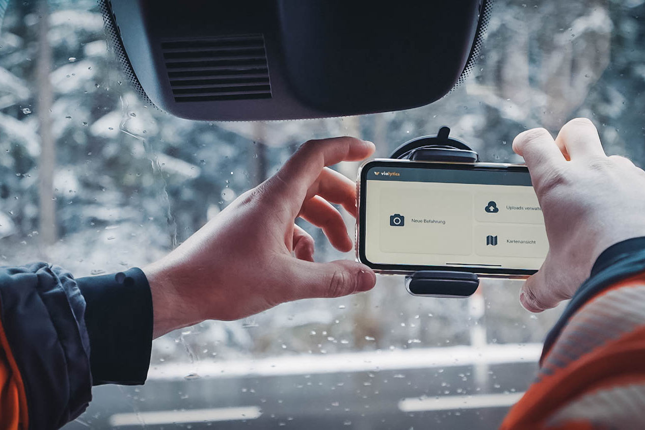 In einem Auto wird ein Handy in eine Halterung an der Windschutzscheibe angebracht. Auf dem Display ist das vialytics System für die Zustandserfassung zu sehen